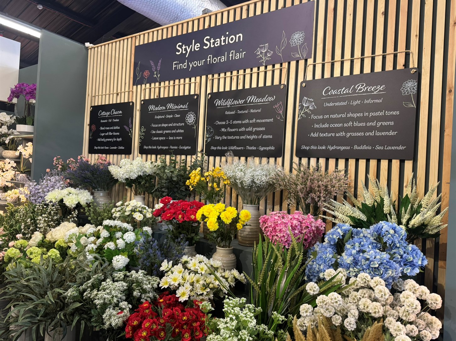 Artificial flower merchandising display showing a style station of flowers and how to use them